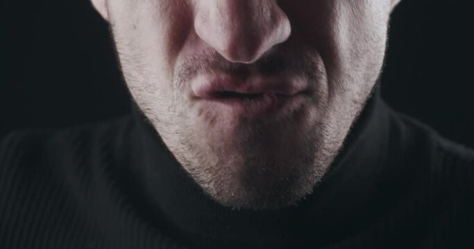 Close-up mouth of angry man screaming. Aggressive male yelling with hate on black background. Danger Violence