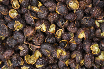 Macro full frame closeup of raw brown whole chinese sichuan timut pepper corns with citrus anise...