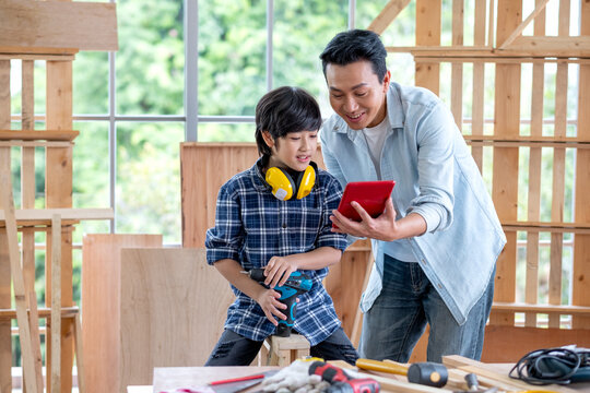 Asian man hold and show tablet to boy and they look happy during carpentering work in their house.