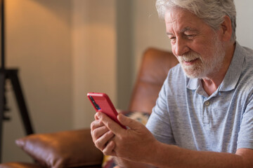 Happy senior handsome man in video call conference using modern smart phone sit down on the sofa at...