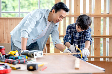 Father help and support his son to practice to use saw in their home workplace.