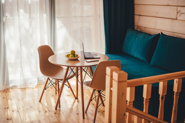 Sunlight illuminates living room workplace home office interior for comfort productive work. on a wooden table a laptop, a mobile phone is charged from a power bank and a green apple. 