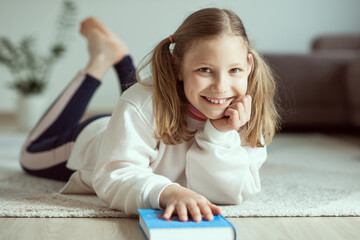 Happy smiling teen girl having fun with book on floor at home