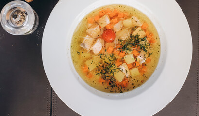 Chicken broth in the white bowl and vegetables on the black wooden background. Top view.Copy space.