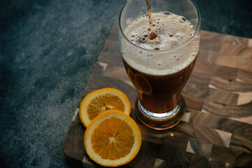 Beer pour in glass with foam on dark moody texture background for adult beverage.