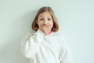 Amazed little girl with widely opend eyes shut her mouth with hand
