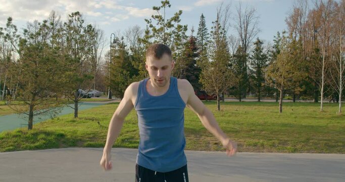 Young muscular man doing physical training outdoors. The guy warms up, stretches his muscles, and then does exercises on parallel bars.