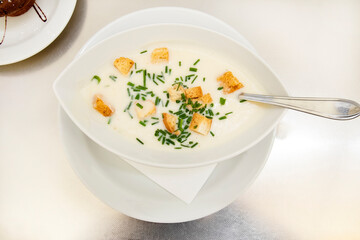 Creamy cream soup with croutons and herbs in a white plate on a table in a restaurant. Gastro tourism after quarantine. Onion cream soup on a table. Cooking at home is tasty during quarantine