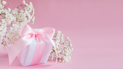 Gift box and a bouquet of blooming gypsophila on a pink background. Mother's day holiday concept. Copy space.