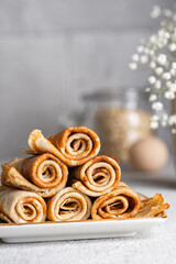 Crepes in rolls on white table. Beautiful breakfast background. Delicious oat pancakes, close up view. Sweet wraps. Organic, healthy dessert, food. Copy space.