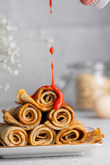 Crepes in rolls with fresh strawberry sauce, white table. Beautiful breakfast background. Delicious...