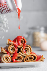 Crepes in rolls with fresh strawberry sauce, white table. Beautiful breakfast background. Delicious...