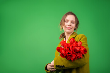 Middle-aged woman smiling with a bouquet of flowers - tulips on a green background. Holiday concept, congratulations.