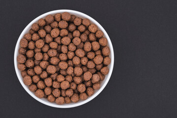 White glass bowl of chocolate corn balls. Isolated on a dark grey background. Top view close up