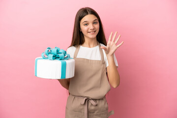 Little girl with a big cake over isolated pink background saluting with hand with happy expression