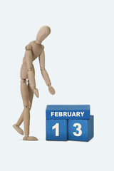 day of the month 13 February calendar . A calendar date on blue cubes and a wooden man standing next to it. White background