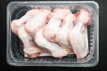 Fototapeta na wymiar Fresh chicken wings spit in plastic vacuum pack, on black stone background, top view flat lay
