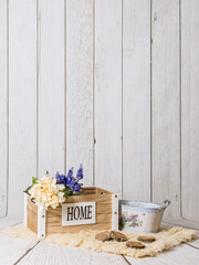 Decoración interior con pared de madera blanca, caja vintage "home" y flores de primavera