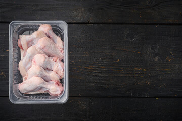 Raw chicken wings in plastic pack, on black wooden table background, top view flat lay, with copy...