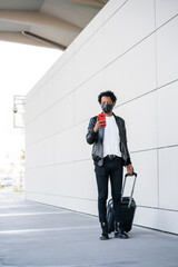 Tourist man using his mobile phone and carrying suitcase outdoors.