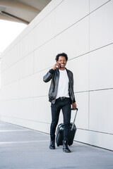 Tourist man talking on phone and carrying suitcase outdoors.