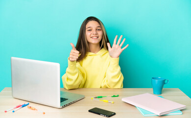 Little girl in a table with a laptop over isolated blue background counting six with fingers