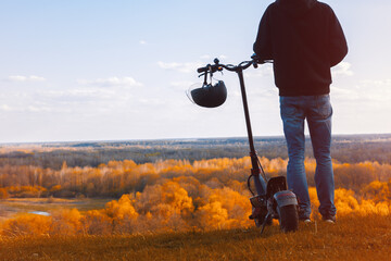 A young man on an electric scooter on the observation deck admires the autumn landscape. Modern urban transport