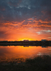 Colorful and dramatic sunset sky reflecting on pond water. Silent evening scene at Delia lake. Vibrant sundown clouds at the horizon over Ungheni city, Moldova. Reed and rush vegetation in the water