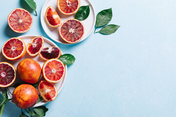 Composition of whole and sliced blood oranges in a plate on light blue table background. Flat lay,...