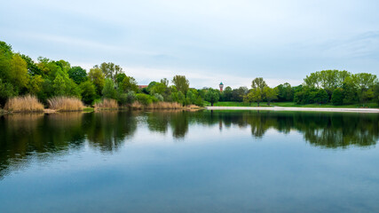 Panoramic landscape at lake in spring, green trees and blue sky symmetrically reflected in water