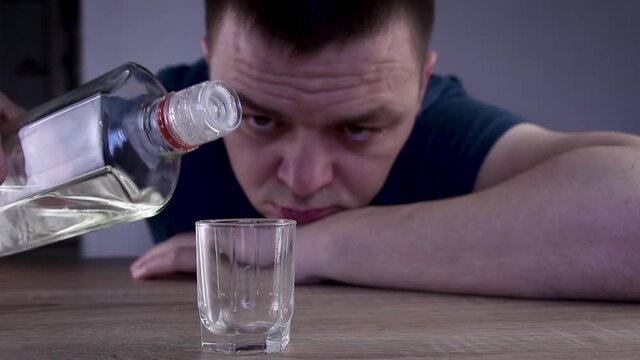 Alcoholic guy drinking cold transparent alcohol drink sake, tequila or rum. Man pouring up frozen vodka from bottle into shot glass .Alcohol dependence addiction