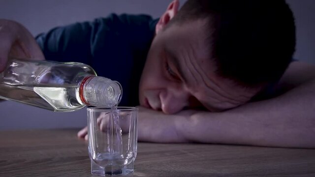 Alcoholic guy drinking cold transparent alcohol drink sake, tequila or rum. Man pouring up frozen vodka from bottle into shot glass .Alcohol dependence addiction