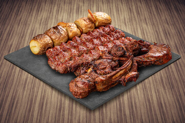 A selection of various barbecued gourmet meats on a black board with a rustic timber background. Rack of lamb, potatoes, kebab