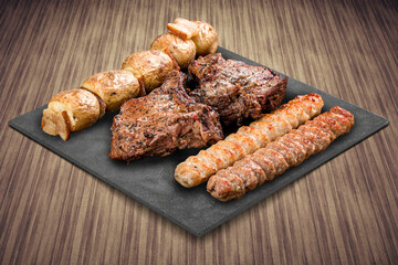 A selection of various barbecued gourmet meats on a black board with a rustic timber background. Pork neck, potatoes, kebab.