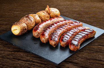 Handmade sausages with baked potatoes on a black board with a rustic timber background.