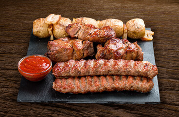 Stone board with different tasty cooked meat on wood background. Pork kebab, lyulya, potatoes.
