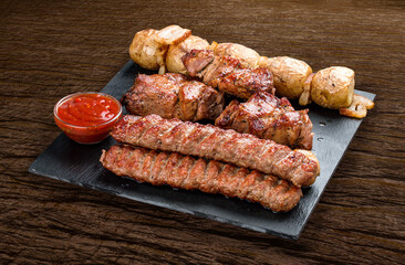 Stone board with different tasty cooked meat on wood background. Pork kebab, lyulya, potatoes.