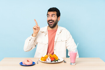 Man at a table having breakfast waffles and a milkshake intending to realizes the solution while lifting a finger up