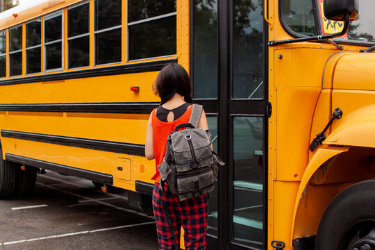 Asian Teen Girl Standing By A Big Yellow School Bus Door With Her Backpack.