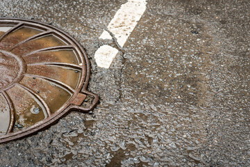Sewer hatch on wet from rain asphalt highway