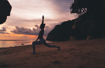 Unrecognizable sportswoman stretching legs on beach during sundown