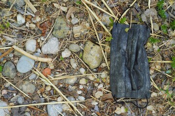 Abandoned mask on ground.  One dirty disposable surgical face mask dropped and discarded in nature. Public health risk, contaminated environment and land pollution.  Environmental problem awareness.