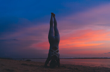 Strong female with athletic body standing on hands and head in asana stretching muscles, woman practice yoga meditation at seashore during evening keeping healthy lifestyle for physical wellness