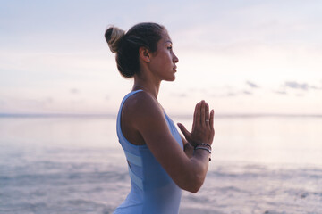 Peaceful ethnic woman doing yoga practice near waterfront in early morning