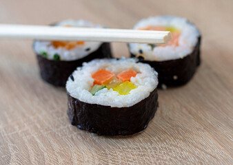 Three sushi rolls with chopsticks on a wooden background