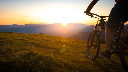 Naklejka na ściany i meble Woman riding mountain bike into the sunset. Beautiful golden summer light.