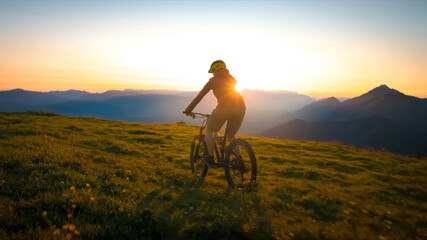 Fototapeta na wymiar Woman riding mountain bike into the sunset. Beautiful golden summer light.
