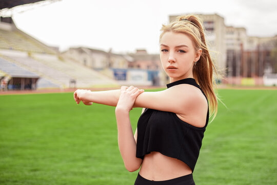 Girl stretches, prepares her body and muscles for a productive fitness workout. Flexible female sporty model on the city stadium. Image with copy space.