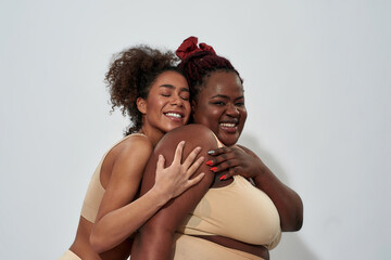 Two smiling african american women in underwear with different body size having fun, posing together isolated over gray background