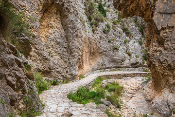 Cobblestone path going through large rocks in a ravine. In the famous Barranc del Cinc de Alcoy, Alicante (Spain)